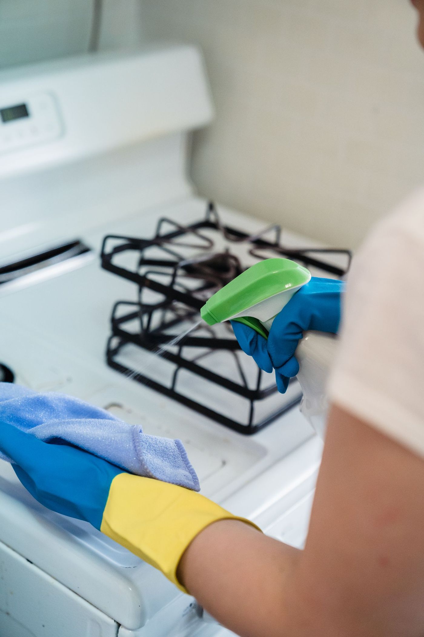 Gloved hands scrubbing a stovetop during a deep cleaning